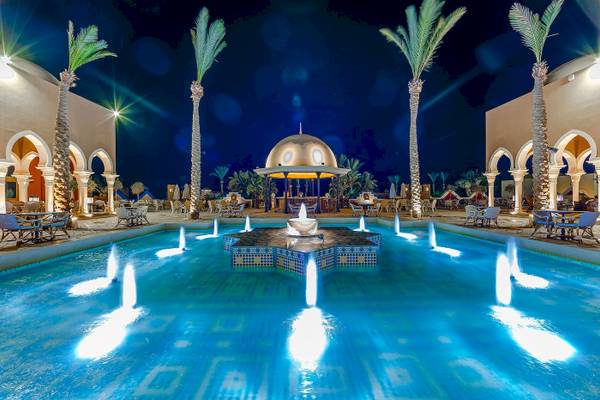 Nachtansicht des Swimmingpools im Grand Makadi Hotel mit Wasserfontaene und umliegenden Liegestuehlen.