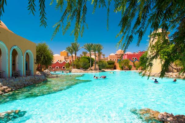 Grand Makadi Hotel zeigt eine große Poollandschaft mit mehreren Schwimmern unter blauem Himmel.