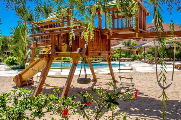 Ein großer hölzerner Spielplatz mit Rutsche und Schaukeln im Freien am Grand Makadi Hotel.