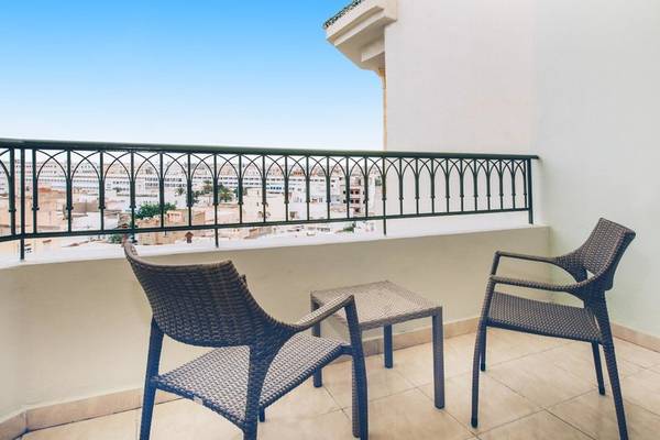 Ein Balkon mit zwei Korbstühlen und einem kleinen Tisch, Blick auf die Stadt.