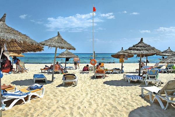 Strandszene mit vielen Sonnenschirmen und Liegestühlen, im Hintergrund das Hotel Paradis Palace.