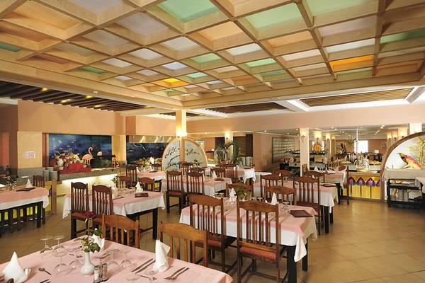 Innenansicht des Restaurants im Paradis Palace Hotel mit gedeckten Tischen, Holzmöbeln und beleuchteter Decke.