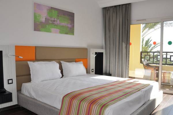 Hotelzimmer im Paradis Palace mit einem Bett, Kissen, einer Decke und einer malerischen Aussicht durch Glastüren.