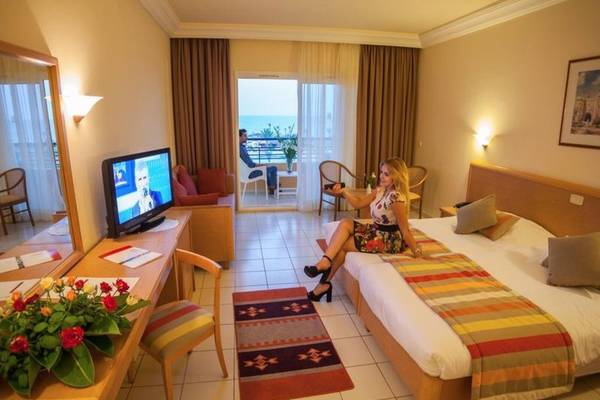 Eine Frau sitzt auf einem Bett im Hotelzimmer des Nour Palace Resort & Thalasso mit Meerblick.