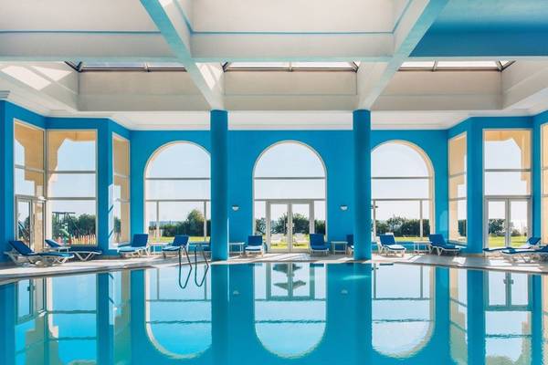 Innenpool des Iberostar Waves Averroes Hotels mit blauen Säulen und Lounge-Stühlen.