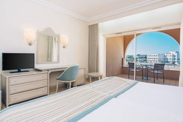 Ein elegantes Zimmer im Iberostar Waves Averroes Hotel mit einem Bett, einem Schreibtisch und einem Balkon mit Blick auf die Stadt.
