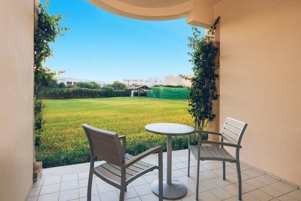 Balkon mit zwei Stühlen und einem Tisch im Iberostar Waves Averroes Hotel mit Blick auf eine große Wiese.