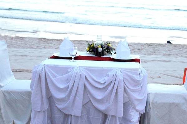 Ein Tisch auf dem Strand mit weißen Tischdecken und Blumen.