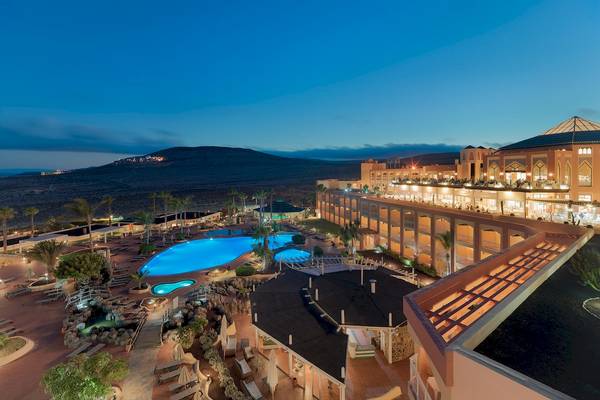 Aussenansicht des H10 Playa Esmeralda Hotels bei Nacht mit Swimmingpool und Bergpanorama.