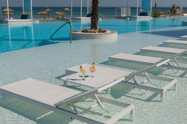 Außenpoolbereich des Iberostar Selection Kuriat Palace Hotels mit weißen Sonnenliegen und Getränken.