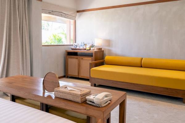 Innenansicht eines Hotelzimmers im Banana Fan Sea Resort mit gelbem Sofa, Tisch und Telefon.