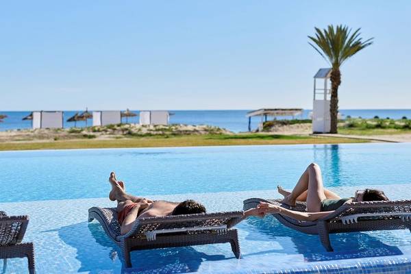 Zwei Personen entspannen auf Liegen am Pool im Iberostar Selection Kantaoui Bay Hotel.