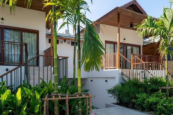 Außenansicht der Villa im Banana Fan Sea Resort mit grünen Pflanzen und hohen Palmen.