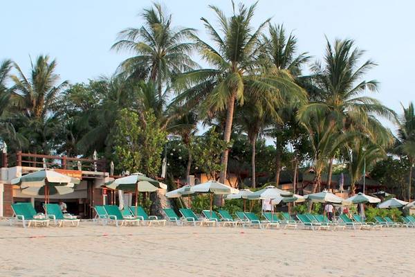 Strand des Banana Fan Sea Resort mit grünen Sonnenliegen und Schirmen, umgeben von Palmen.