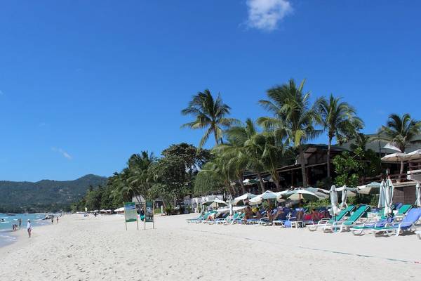 Strandszene des Banana Fan Sea Resorts mit weißen Liegestühlen, Sonnenschirmen und Besuchern.