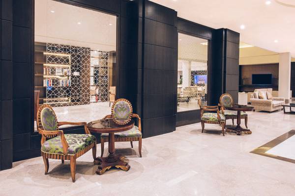 Hotellobby mit kunstvollen Sesseln und Tischen, gerahmt von schwarzen Wänden und großen Glasvorhängen.