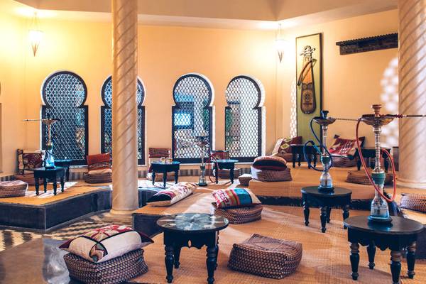 Lounge-Bereich im Iberostar Selection Diar El Andalous mit Wasserpfeifen, Tischen, Kissen und orientalischen Fenstern.