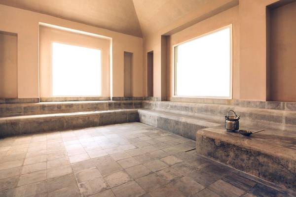 Eine leere Sauna im Iberostar Selection Diar El Andalous Hotel mit gefliesten Wänden und Boden, zwei großen Fenstern und einem kleinen Tisch.