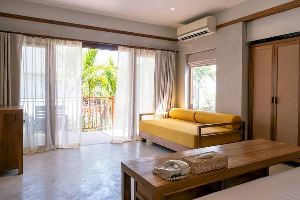 Innenansicht eines Zimmers im Banana Fan Sea Resort mit gelbem Sofa, Balkon und großen Fenstern.