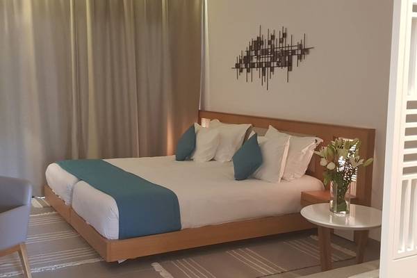 Doppelbett im Hotelzimmer der Orangers Garden Villas & Bungalows mit weißen und blauen Kissen und einem Nachttisch mit Blumen.