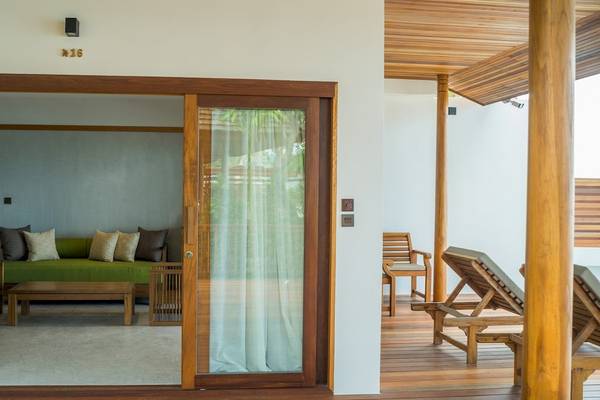 Innenansicht des Wohnbereichs des Banana Fan Sea Resort mit einem grünen Sofa, Kissen, einem Tisch und hölzernen Möbeln auf einer Terrasse.