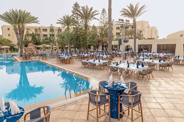 Außenbereich des Aldiana Club Djerba Atlantide mit Swimmingpool und gedeckten Tischen.