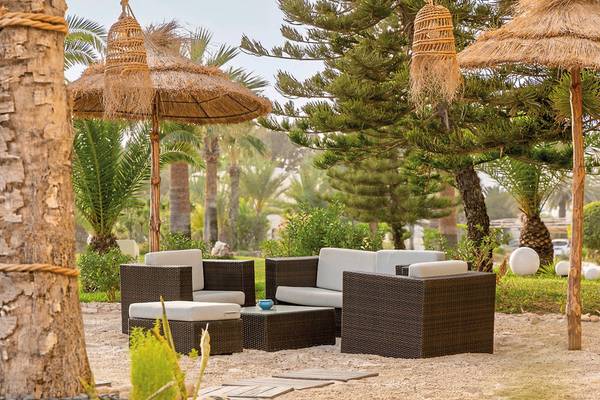 Gartenmöbel im Aldiana Club Djerba Atlantide Hotel, umgeben von Bäumen und Pflanzen.