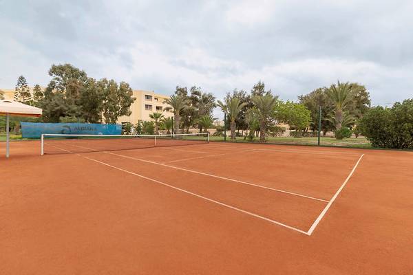 Tennisplatz im Aldiana Club Djerba Atlantide mit Gebäuden und Bäumen im Hintergrund.