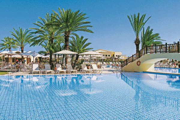 Ein Swimmingpool im Aldiana Club Djerba Atlantide Hotel, umgeben von Palmen und Sonnenliegen.