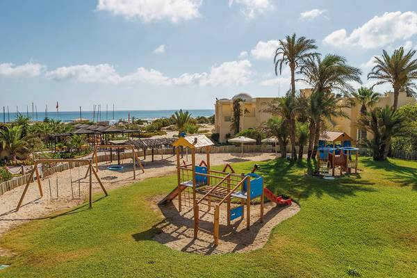 Außenansicht des Kinderspielplatzes im Aldiana Club Djerba Atlantide mit Spielgeräten und Gebäuden im Hintergrund.