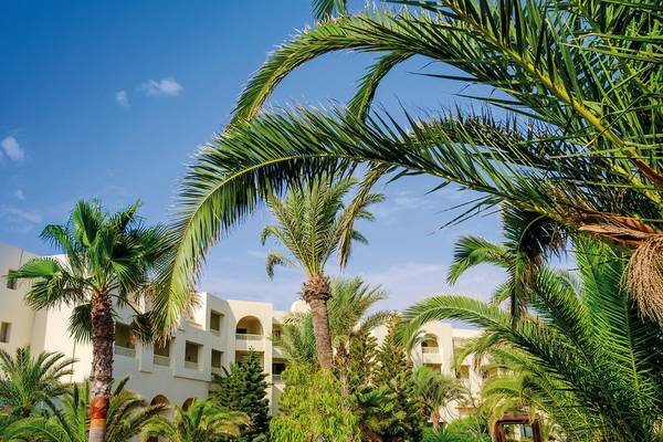 Palmen und Gebäude des Aldiana Club Djerba Atlantide Hotels unter blauem Himmel