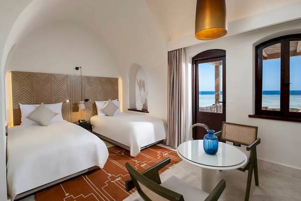 Doppelzimmer mit Meerblick im Mövenpick Resort El Quseir, mit zwei Betten, Tisch, Stühlen und Fenstern mit Meersicht.