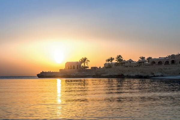 Sonnenuntergang am Mövenpick Resort El Quseir am Meer mit Gebäuden und Palmen
