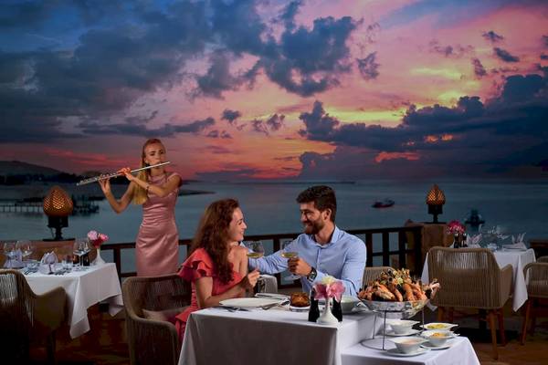 Paar genießt romantisches Essen auf einer Terrasse mit Blick auf die Flut und einer Musikerin.