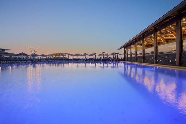 Poolbereich des Arina Beach Resorts bei Sonnenuntergang mit blau beleuchtetem Wasser und Sonnenliegen.