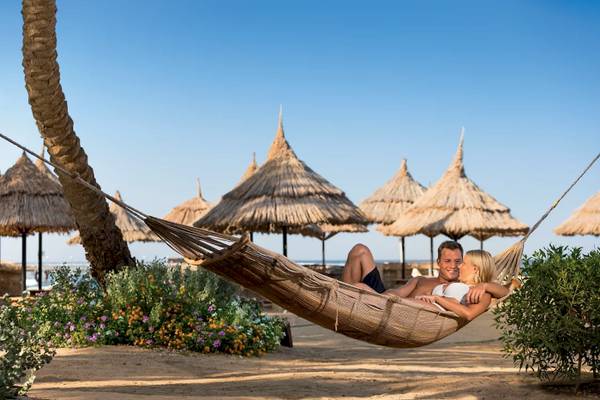 Paar im Hammock im Mövenpick Resort El Quseir mit Blick auf das Meer und Strohhütten.