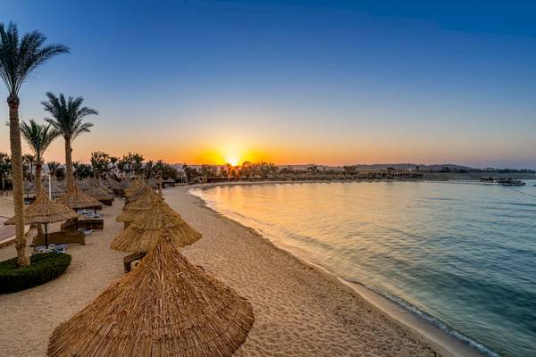Sonnenuntergang am Strand des Mövenpick Resorts El Quseir mit Palmen und Sonnenschirmen