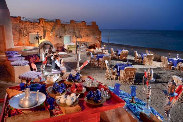 Abendansicht des Strandrestaurants im Mövenpick Resort El Quseir mit blauen Tischdecken und Stühle am Meer.
