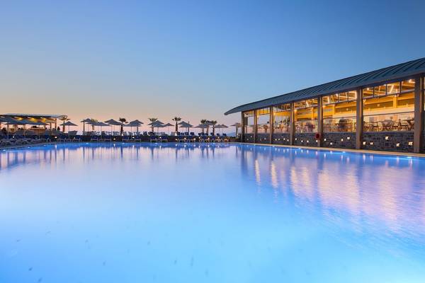 Außenpool des Arina Beach Resorts bei Sonnenuntergang mit Lounge-Stühlen und Sonnenschirmen.