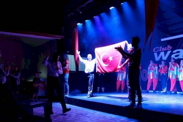 Feier auf der Bühne im Club Wasa Holiday Dorf mit einer Gruppe in roten Overalls, die eine türkische Flagge halten.