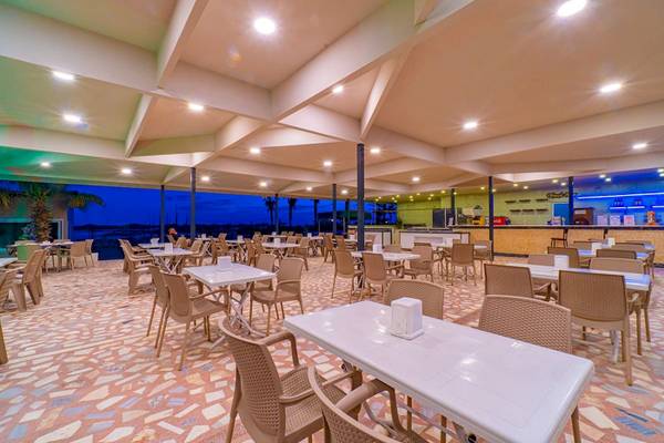 Innenbereich des Club Wasa Holiday Village Restaurants mit Tischen und Stühlen, hellem Dekor und Blick auf die Nachtlandschaft.