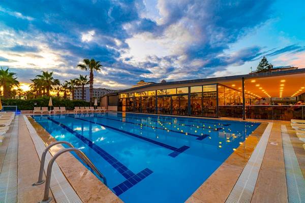 Außenpool des Club Wasa Holiday Village bei Sonnenuntergang mit Lounge-Stühlen und Palmen