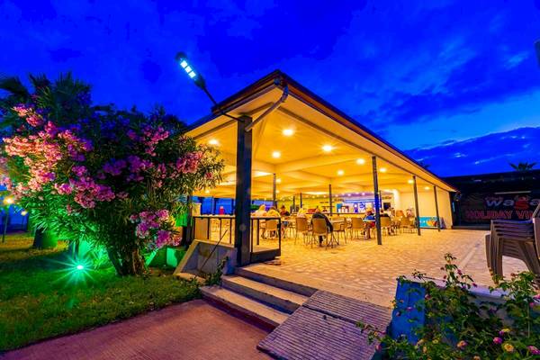Terrasse des Club Wasa Holiday Village bei Nacht mit beleuchteten Pflanzen und Gästen.
