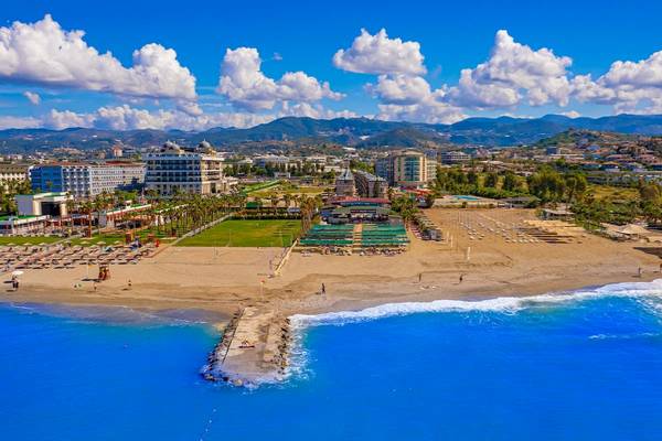 Luftaufnahme des Club Wasa Holiday Village mit Strand, Gebäuden und Bergen im Hintergrund.