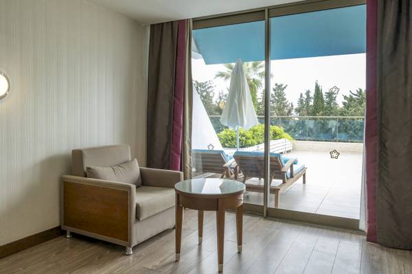 Innenraum des Side Star Elegance Hotels mit einem gemütlichen Sessel, einem kleinen Tisch und einer großen Glastür, die auf eine Terrasse mit Sonnenliegen führt.