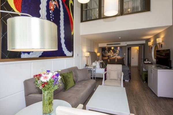 Innenraum der Suite im Side Star Elegance Hotel mit Wohnzimmer, Couch, Tisch, Sessel, Fernseher und Kunstwerk.