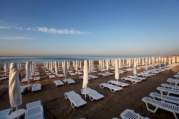 Ein Strand mit vielen weißen Sonnenliegen und Sonnenschirmen am Meer