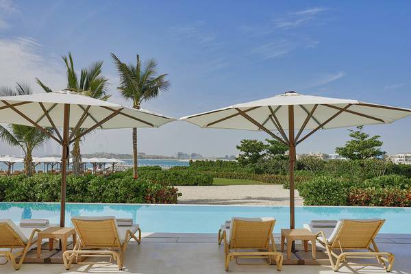 Loungebereich am Pool des NH Collection Dubai The Palm mit weißen Sonnenschirmen und Strandkörben.
