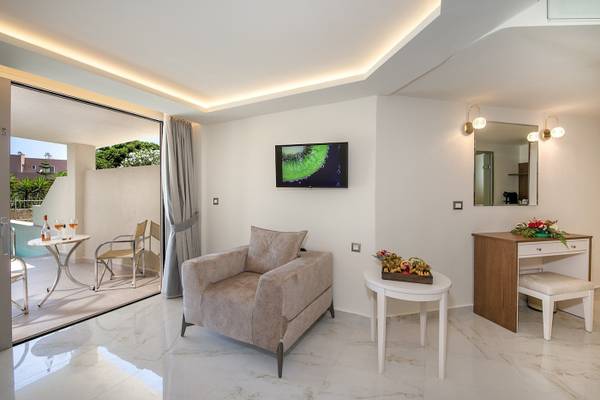 Innenansicht einer Suite im Vantaris Luxury Beach Resort mit Fernseher, Tisch, Stühlen und Dekor.