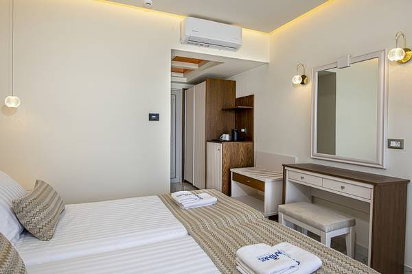 Interieur eines Hotelzimmers im Vantaris Luxury Beach Resort mit zwei Betten, Kleiderschrank und Klimaanlage.